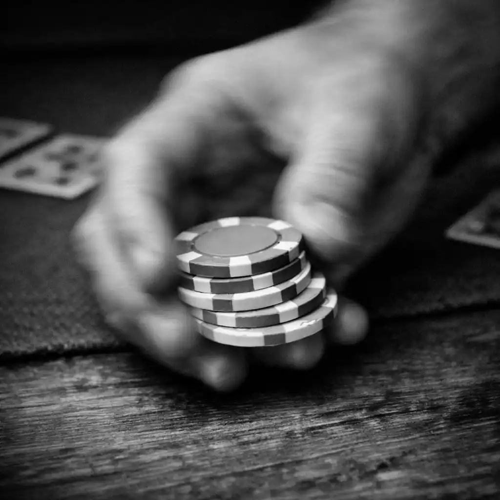 Gros plan d’une main tenant des jetons de poker en céramique au-dessus d’une table en bois, avec tapis de jeu en feutre